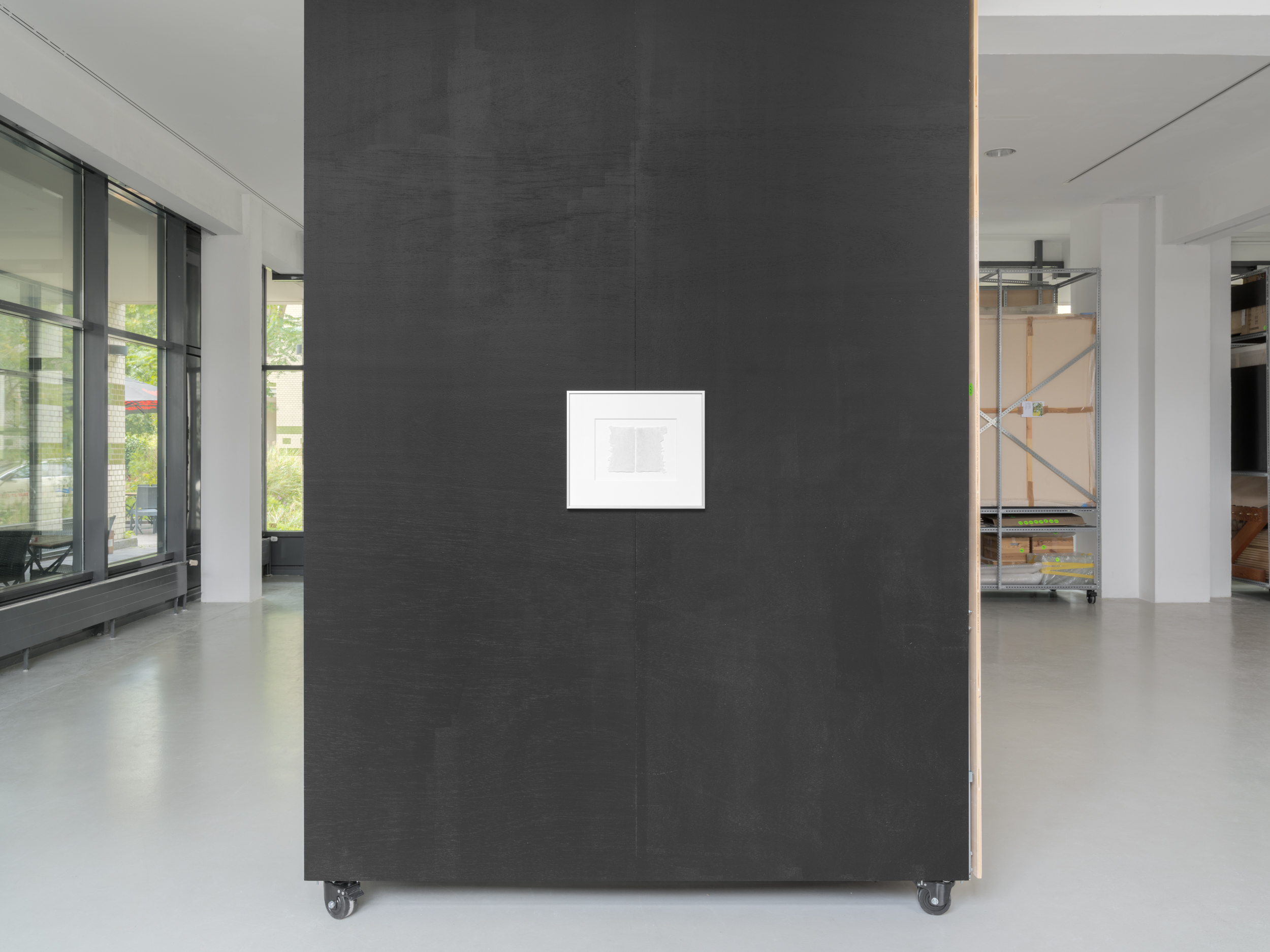 Aisha Altenhofen solo exhibition at Austin Space: Installation view towards the door with a warmer light temperature, a small photographic work hangs on the opposite wall to a grid light fixture that is hung on the wall.